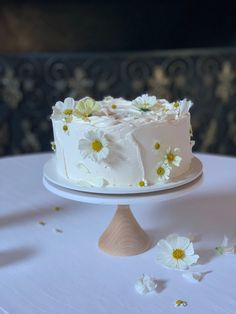 a white cake sitting on top of a table with daisies around it and flowers