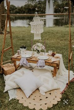 a picnic table with plates and drinks on it in the grass next to a lake