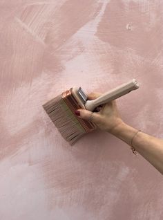 a person is holding a brush with pink paint on the wall behind them and it looks like they are painting