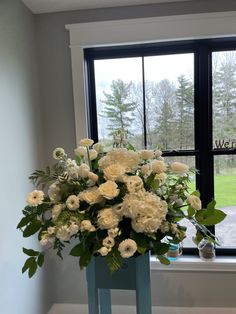 a vase filled with white flowers on top of a blue table next to a window