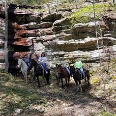 four people are riding horses on a trail in the woods near some large rock formations