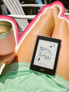 a woman laying on the beach with her legs crossed and holding a book