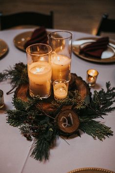 candles are lit on top of a wooden slice with evergreen branches and pine cones around it