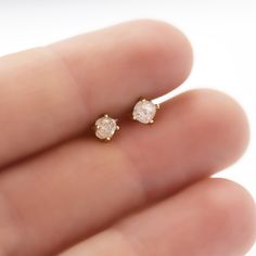 a person's hand holding two small diamond earrings