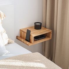 a small wooden shelf on the side of a bed next to a phone and cup