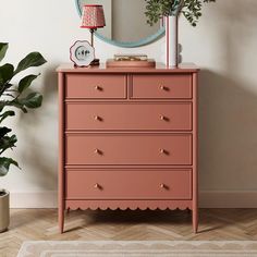 a pink dresser with gold knobs in front of a mirror and potted plant