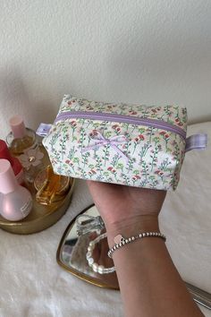 a hand holding a small white bag next to a mirror and other personal care items