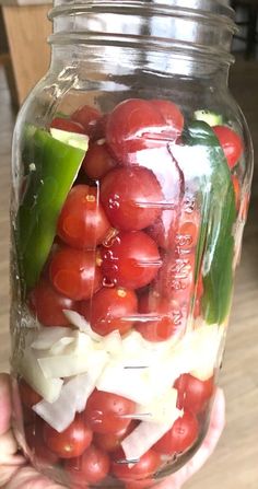 a person holding a jar filled with tomatoes and cucumbers