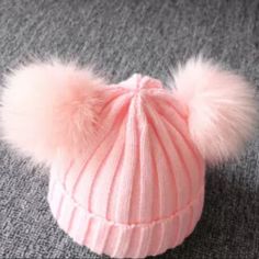 a pink hat with white pom - poms sitting on top of a carpet