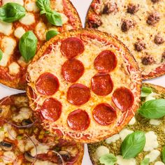 four different types of pizzas with basil leaves on the top and one pepperoni