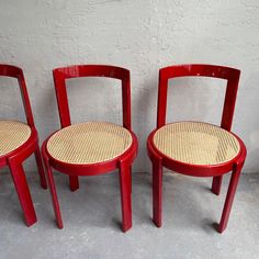 three red chairs sitting next to each other in front of a white wall and floor