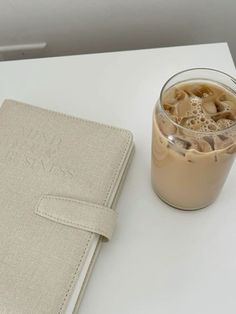 a cup of iced coffee next to a book on a table with a drink in it