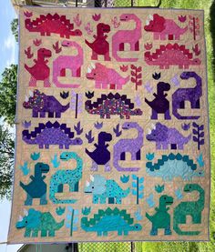 a quilted wall hanging on the side of a building with dinosaurs and trees in it