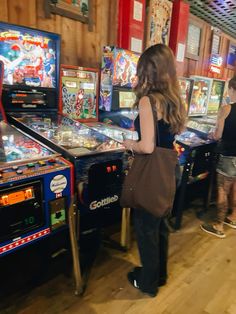 two women are playing pinball in a room full of arcade machines and other games