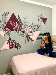 a woman sitting on top of a bed next to a wall with flowers and leaves