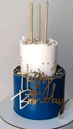 a blue and white birthday cake with gold candles on it's top that says happy birthday