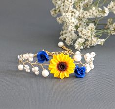 a yellow sunflower and blue roses on a gold chain bracelet with pearls, beads and flowers