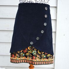 a blue skirt with buttons on it hanging from a wooden pole in front of a white house