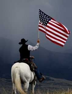 a man riding on the back of a white horse holding an american flag in his hand