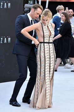 a man and woman standing next to each other in front of a black wall with an open back dress