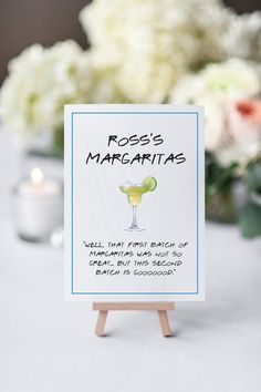 a sign that says ross's margarita station is on a table with flowers in the background