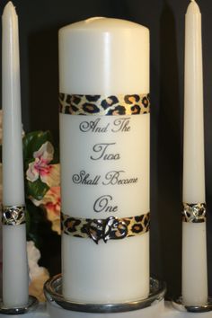 two white candles sitting on top of a table next to each other with leopard print ribbon around them