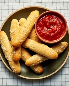 some bread sticks are on a plate with ketchup and sauce in the bowl