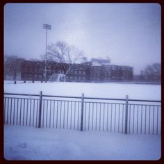 a snow covered field with a fence and some buildings in the backgroung