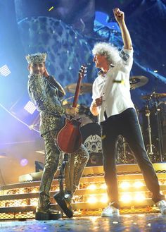 two men on stage with guitars and one holding his hand up in the air as he sings