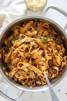 a pan filled with pasta and meat on top of a table next to a spoon