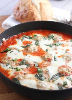 a pan filled with meatballs and sauce on top of a wooden table next to bread