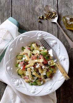 a white bowl filled with pasta and vegetables on top of a table next to utensils