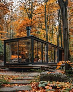 a glass cabin in the woods surrounded by trees with fall foliage and leaves on the ground