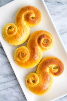 three rolls on a white plate sitting on a marble counter top next to a cup of coffee