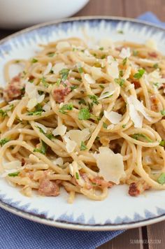 a plate of pasta with parmesan cheese and bacon on top, sitting on a blue napkin