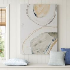 an abstract painting hangs on the wall above a white bench with pillows and throw pillows