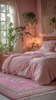 a bed with pink sheets and pillows next to a window filled with potted plants