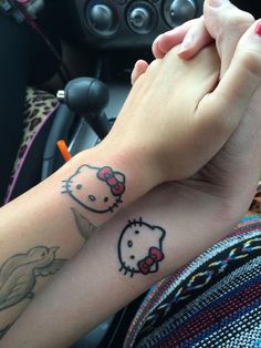 two people holding hands with hello kitty tattoos on their wrist and wristbands in the car