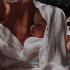 a woman holding a baby wrapped in a white blanket on top of a bed next to flowers