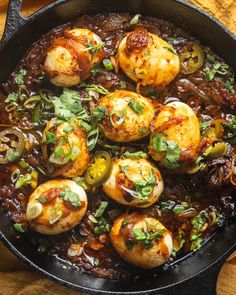 an iron skillet filled with cooked scallops covered in sauce and garnished with fresh herbs