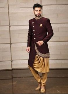 a man standing in front of a garage door wearing a maroon and gold sherwani