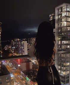 a woman standing on top of a tall building looking at the city lights in the distance