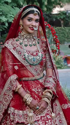 a woman in a red and gold bridal outfit with jewelry on her head, standing outside