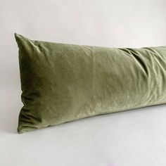 an olive green velvet pillow on a white background with the back turned up to show it's curved edges