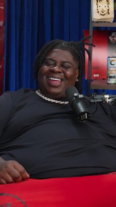 a woman sitting in front of a microphone on top of a red couch next to a blue curtain