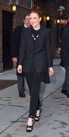 a woman in a black suit is walking down the street