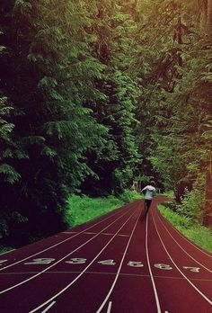 a man is running on a track in the middle of a forest with trees behind him