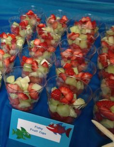 fruit cups with strawberries and other fruits in them on a blue table cloth next to starfish