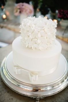 a wedding cake with white flowers on top sitting on a silver platter in the middle of a table