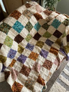 a multicolored blanket sitting on top of a bed next to a potted plant